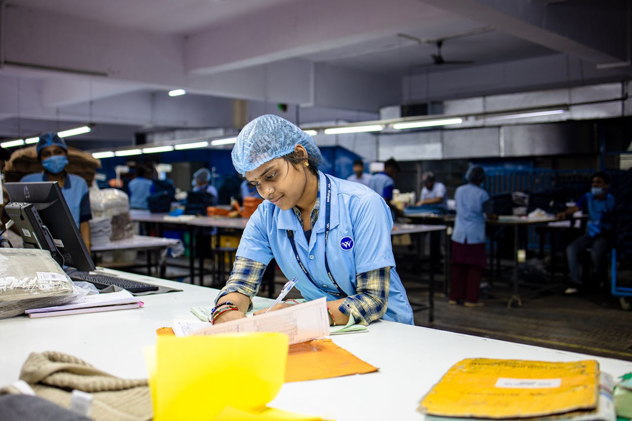 mobile-01 Female factory worker wearing uniform and hairnet, focused on writing tasks in textile environment.