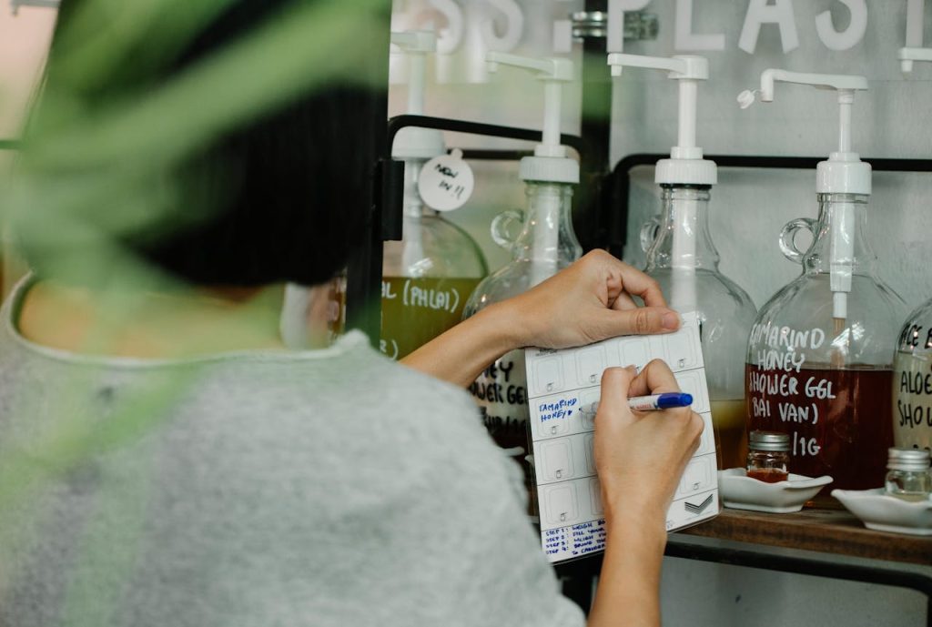 person-writing-on-paper-7262690 Person using a pen to take notes in an eco-friendly refill store with glass containers.