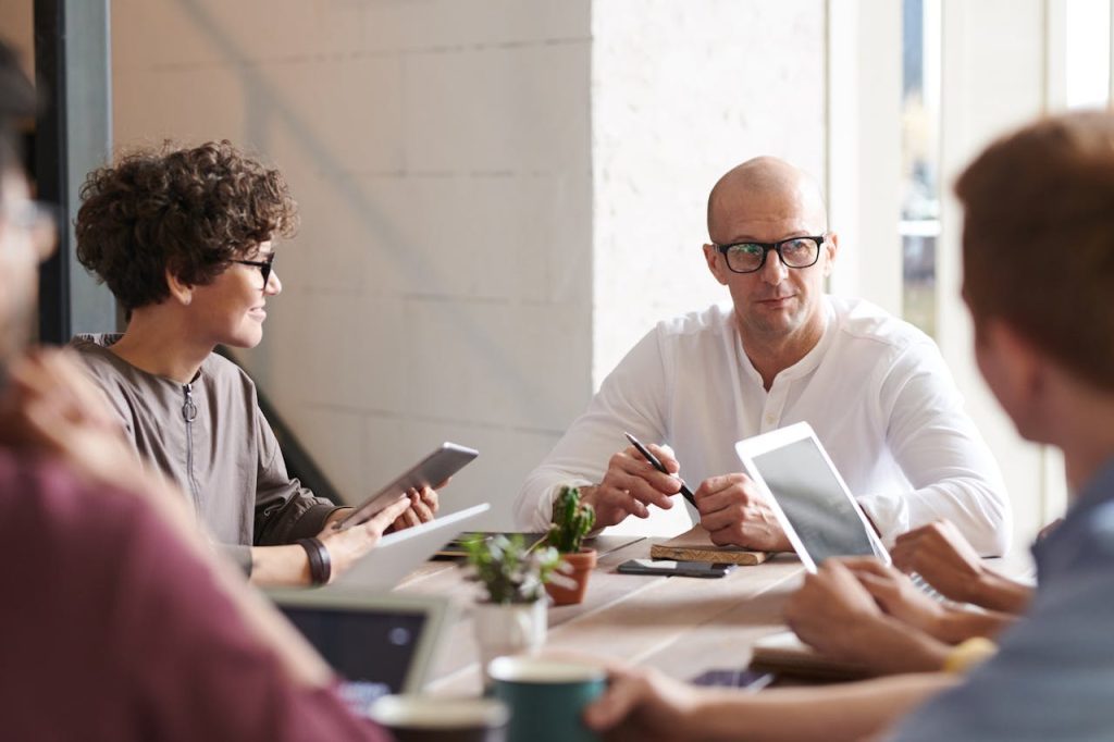 photo-of-man-sitting-in-front-of-people-3184299 Group of professionals engaged in a brainstorming session around a table in a contemporary office space.